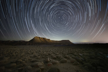 Star trails over the desert landscape, mountain and stones field