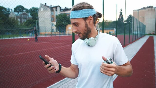 Handsome sportsman training with hand espander and typing messages in social media on smartphone. Active fitness guy. Workout. Training concept.
