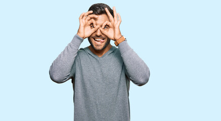 Handsome hispanic man wearing casual clothes doing ok gesture like binoculars sticking tongue out, eyes looking through fingers. crazy expression.