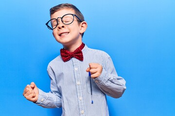 Cute blond kid wearing nerd bow tie and glasses very happy and excited doing winner gesture with...
