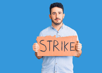 Young hispanic man holding strike banner cardboard thinking attitude and sober expression looking self confident