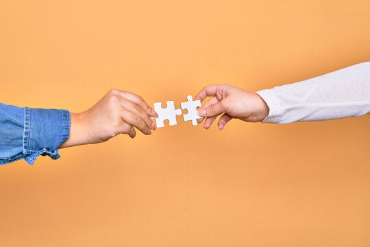 Hands of caucasian young people connecting pieces of puzzle over isolated yellow background