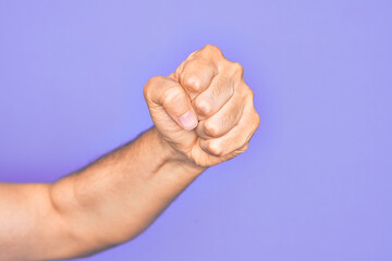 Hand of caucasian young man showing fingers over isolated purple background doing protest and revolution gesture, fist expressing force and power