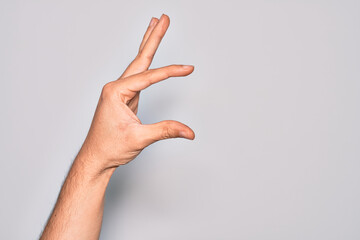 Hand of caucasian young man showing fingers over isolated white background picking and taking invisible thing, holding object with fingers showing space