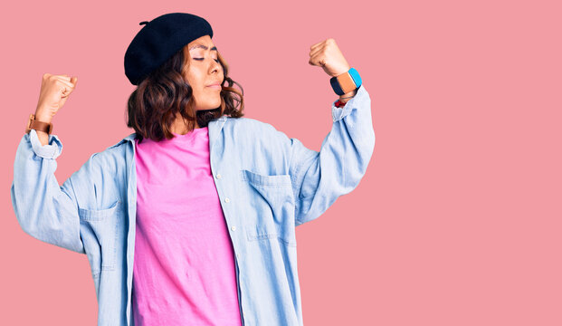 Young beautiful mixed race woman wearing french look with beret showing arms muscles smiling proud. fitness concept.