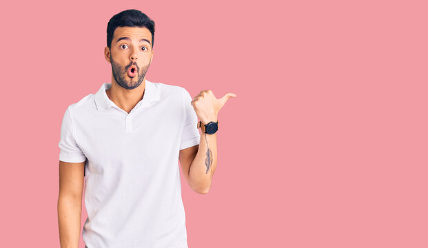 Young handsome hispanic man wearing casual clothes surprised pointing with hand finger to the side, open mouth amazed expression.