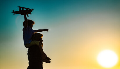 Fototapeta na wymiar Success and child leader concept. Sunset silhouette of Father and son together. Boy child is sitting on daddy shoulder piggyback while the flight.
