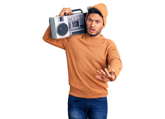 Handsome latin american young man holding boombox, listening to music doing stop gesture with hands palms, angry and frustration expression