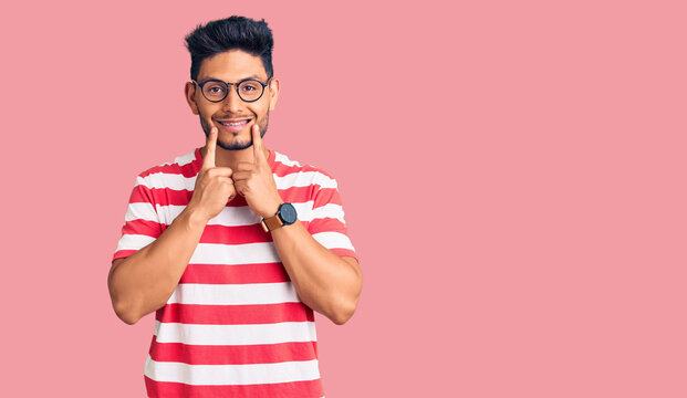 Handsome latin american young man wearing casual clothes and glasses smiling with open mouth, fingers pointing and forcing cheerful smile