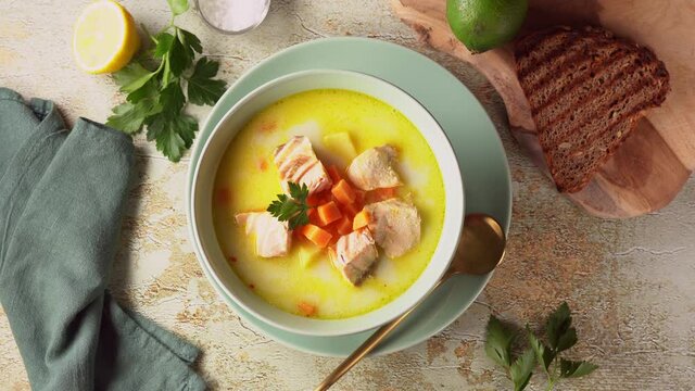 Delicious salmon chowder soup with carrots, potatoes and parsley in a green plate seeing from above. Rotation from right to left. 4K UHD