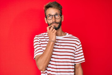 Handsome caucasian man with beard wearing casual clothes and glasses serious face thinking about question with hand on chin, thoughtful about confusing idea