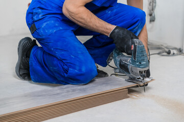 Woodworker in blue uniform cuts laminate flooring with a jigsaw. Close up