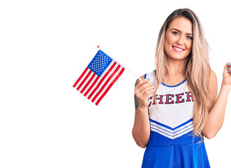 Young beautiful blonde woman wearing cheerleader uniform holding united states flag smiling happy...