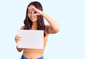 Young beautiful chinese girl holding paper banner with blank space smiling happy doing ok sign with hand on eye looking through fingers