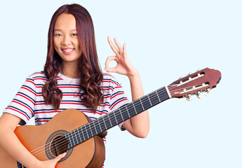 Fototapeta premium Young beautiful chinese girl playing classical guitar doing ok sign with fingers, smiling friendly gesturing excellent symbol