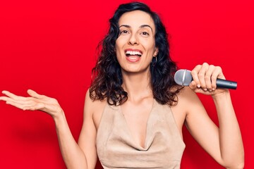 Obraz premium Young beautiful hispanic woman singing song using microphone celebrating achievement with happy smile and winner expression with raised hand