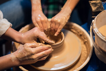close-up of the hands of a Potter's girl and a child who are sculpting clay dishes on a Potter's wheel