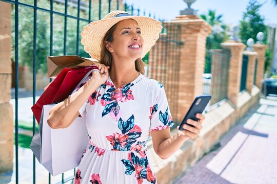 Middle age woman holding shopping bags and using smartphone at the city