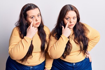 Young plus size twins wearing casual clothes pointing to the eye watching you gesture, suspicious expression