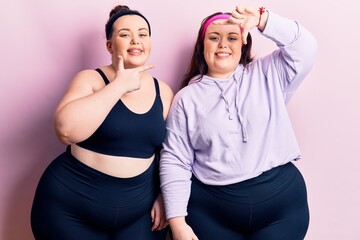 Obraz premium Young plus size twins wearing sportswear smiling making frame with hands and fingers with happy face. creativity and photography concept.
