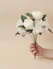 artificial branches of flowers in female hand on beige monochromatic background