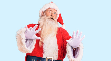 Old senior man with grey hair and long beard wearing traditional santa claus costume afraid and terrified with fear expression stop gesture with hands, shouting in shock. panic concept.