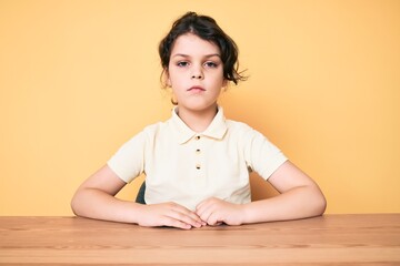 Cute hispanic child wearing casual clothes sitting on the table with serious expression on face. simple and natural looking at the camera.