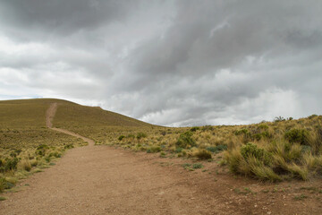 The dirt path along the hill and yellow grassland under a cloudy sky. 