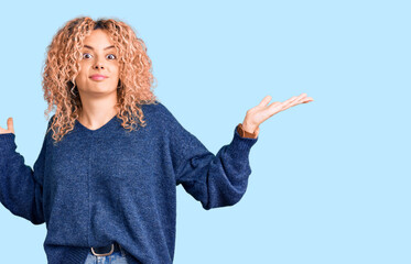 Young blonde woman with curly hair wearing casual winter sweater clueless and confused expression...