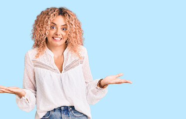 Young blonde woman with curly hair wearing elegant summer shirt clueless and confused expression...