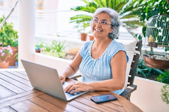 Middle age woman with grey hair smiling happy relaxing sitting at the terrace working from home