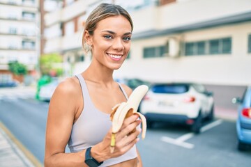 Young cauciasian fitness woman wearing sport clothes training outdoors eating healthy banana for strength and energy - obrazy, fototapety, plakaty