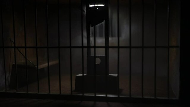Execution concept. Death penalty guillotine miniature inside old prison. Old prison bars cell lock. Man inside jail. Horror view of Guillotine scale model in the dark