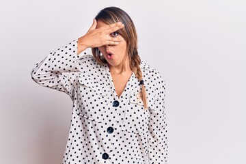 Young beautiful woman wearing casual dress peeking in shock covering face and eyes with hand, looking through fingers afraid