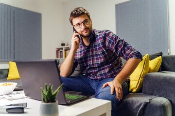 Young adult entrepreneur or businessman working form home late at night - Man sitting on the couch sofa at his apartment making a phone call listening