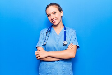 Young blonde woman wearing doctor uniform and stethoscope happy face smiling with crossed arms...