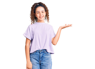 Beautiful kid girl with curly hair wearing casual clothes smiling cheerful presenting and pointing with palm of hand looking at the camera.