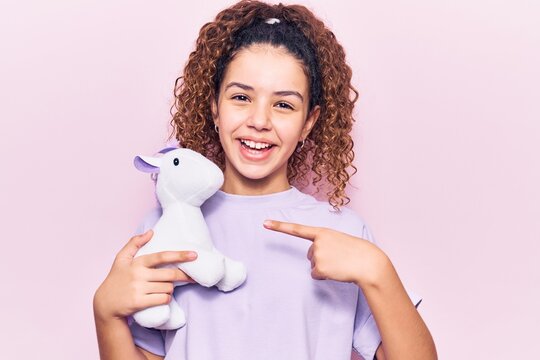 Beautiful kid girl with curly hair holding animal doll toy smiling happy pointing with hand and finger