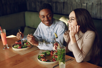 Black man in a cafe. International people. Man in a blue shirt. Woman drinking a cocktails. People with a salad.