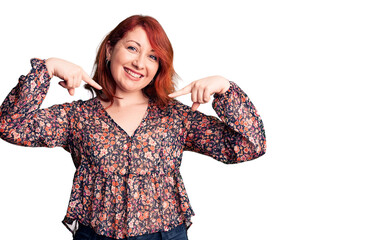 Young beautiful redhead woman wearing casual t-shirt looking confident with smile on face, pointing...