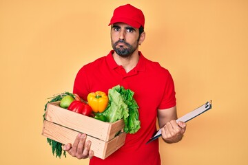 Handsome hispanic man with beard wearing uniform holding delivery food skeptic and nervous,...