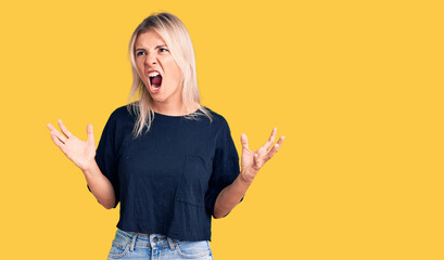 Young beautiful blonde woman wearing casual t-shirt crazy and mad shouting and yelling with aggressive expression and arms raised. frustration concept.