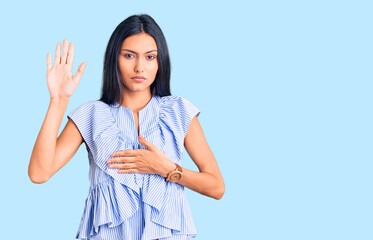 Young beautiful latin girl wearing casual clothes swearing with hand on chest and open palm, making...