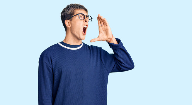 Young handsome man wearing casual clothes and glasses shouting and screaming loud to side with hand on mouth. communication concept.