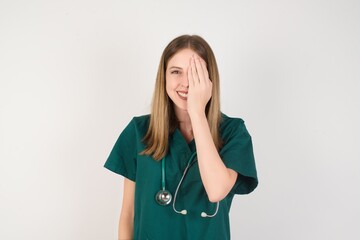 Female doctor wearing a green scrubs and stethoscope covering one eye with her hand, confident smile on face and surprise emotion.