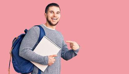 Young handsome man wearing student backpack holding notebook smiling happy pointing with hand and finger
