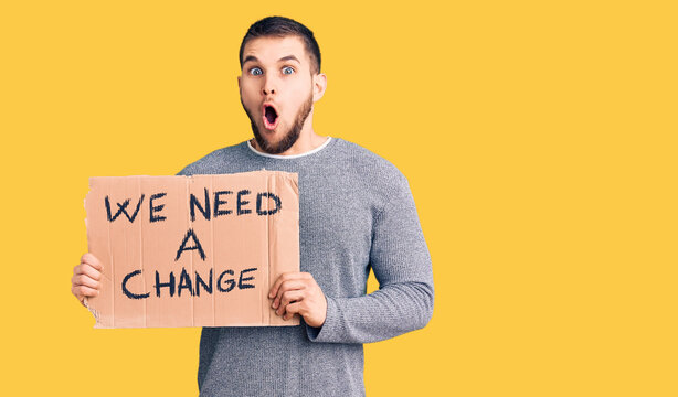 Young handsome man holding we need a change banner scared and amazed with open mouth for surprise, disbelief face