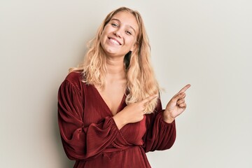 Young blonde girl wearing casual clothes smiling and looking at the camera pointing with two hands and fingers to the side.