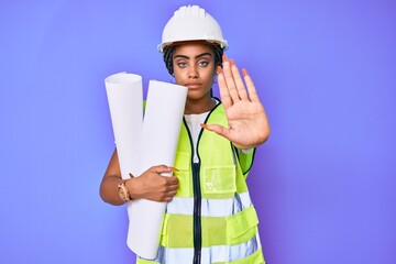 Young african american woman with braids wearing safety helmet holding blueprints with open hand doing stop sign with serious and confident expression, defense gesture
