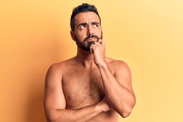 Fototapeta premium Young hispanic man standing shirtless serious face thinking about question with hand on chin, thoughtful about confusing idea